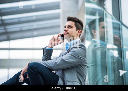 Un Ritratto di giovane imprenditore con seduta dello smartphone nel corridoio al di fuori ufficio. Foto Stock