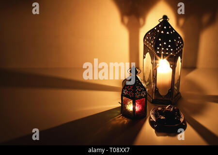 Arabo ornamentali lanterne e candele accese incandescente durante la notte. Piastra con data di frutta sul tavolo. Golden festosa bigliettino, invito per musulmani Foto Stock