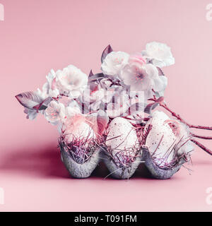 Uova di Pasqua in griglia con le piume e la primavera sbocciano i fiori a pastello sfondo rosa Foto Stock