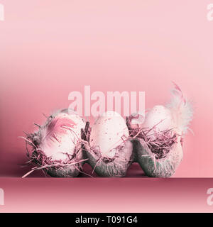Uova di Pasqua in griglia con le piume a pastello sfondo rosa Foto Stock