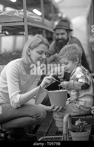 La mamma che mostra il suo figlio foglie di piccolo fiore rosa caldo pot tenendo premuto il giardinaggio vanga. Famiglia lavorando insieme in serra Foto Stock