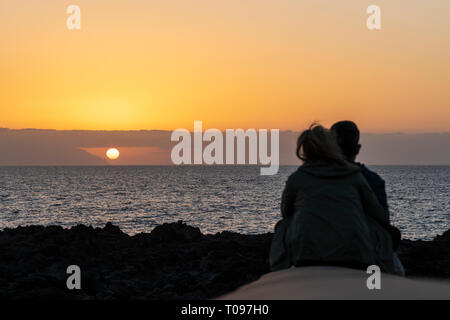 Giovane seduto su una parete a guardare il tramonto visto da Playa de la Arena sulla costa occidentale di Tenerife, Isole Canarie, Spagna Foto Stock