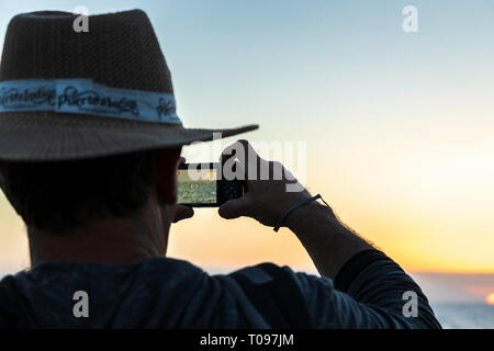 L'uomo con il cappello di paglia per fotografare il tramonto visto da Playa de la Arena sulla costa occidentale di Tenerife, Isole Canarie, Spagna Foto Stock