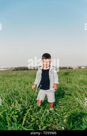 Happy little boy camminando su erba in estate giornata soleggiata nel campo Foto Stock