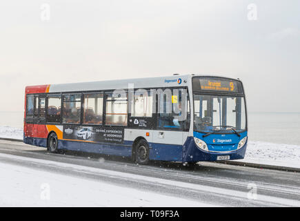 I mezzi di trasporto pubblici Stagecoach bus su una neve ghiacciata strada coperta mentre nevica nel West Sussex, in Inghilterra, Regno Unito. Foto Stock