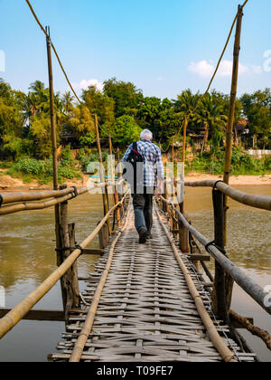 Senior maschio passeggiate turistiche attraverso traballanti di canna di bambù ponte sul Nam Kahn fiume affluente del Mekong, Luang Prabang, Laos, Indocina, SE Asia Foto Stock