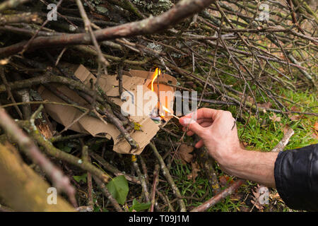 Impostazione di mano il fuoco con un fiammifero acceso per avviare la masterizzazione di un nazionale di falò per bruciare le foglie e ramoscelli, acceso in un giardino interno in campagna. (104) Foto Stock