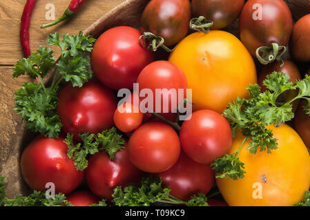 Close up di pomodori organico con alcune imperfezioni naturali, verde con prezzemolo e peperoni rossi. In legno naturale la superficie del tavolo. Messa a fuoco selettiva. Healt Foto Stock