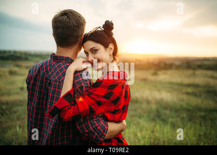 Felice amore giovane abbraccia in campo estivo al tramonto. Giuncata romantica di un uomo e di una donna, picnic sul prato Foto Stock