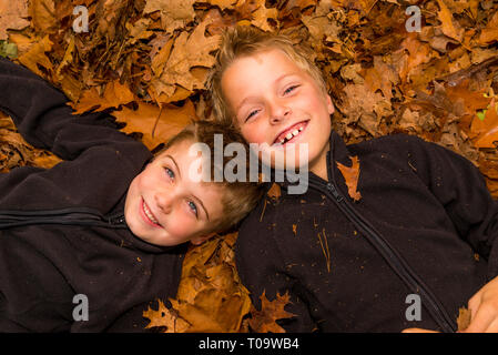 Kwo kids posa in un mucchio di foglie Foto Stock