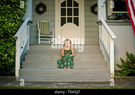 Ritratto di un felice giovane ragazza seduta sui gradini di fronte di una casa suburbana. Foto Stock