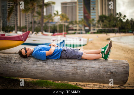 Ragazzo adolescente giacente su un tronco di albero su una spiaggia. Foto Stock