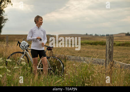 Sorridente donna matura prendendo una pausa dal bike per ammirare un campo rurale. Foto Stock