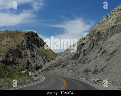 Strada asfaltata che sparisce dietro le affilate montagne rocciose al Parco Nazionale di Yellowstone nel Wyoming, USA. Foto Stock