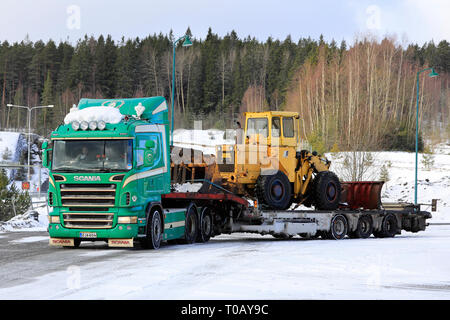 Salo, Finlandia - 9 Marzo 2019: Verde Scania carrello Noteboom con rimorchio a pianale ribassato che trasportano il vecchio caricatore su ruote pronto per il trasporto in un giorno d'inverno. Foto Stock