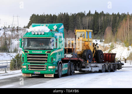 Salo, Finlandia - 9 Marzo 2019: Verde Scania carrello Noteboom con rimorchio a pianale ribassato che trasportano il vecchio caricatore su ruote pronto per il trasporto in un giorno d'inverno. Foto Stock