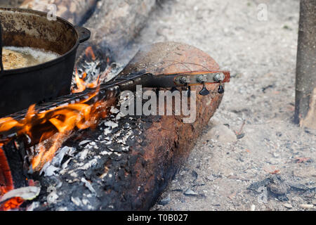 La masterizzazione di collo della chitarra e vecchio fuligginosa calderone sul fuoco a forest Foto Stock