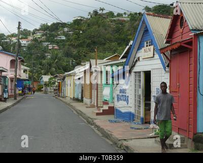 LUCIA, nelle Isole dei Caraibi-MARZO 2017: Un uomo cammina lungo la strada con le righe del vecchio in legno case in legno su Church Street nella città di Soufriere, St. Lucia Foto Stock