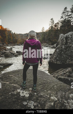 Una giovane donna si erge, ammirando il fiume dopo una escursione in un viola Arc'teryx giacca. Foto Stock