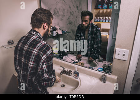 Un giovane uomo si lava le mani in un bagno pulito mentre la sua riflessione unkempt guarda a se stesso mentre in piedi in un bagno sporco. Foto Stock