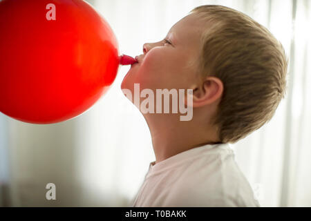 Felice ragazzo avendo divertimento che soffia su un palloncino rosso. Foto Stock
