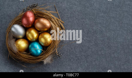 Felice Pasqua messaggio di saluto festivo simbolo elegante in legno naturale nido di erba con colorate uova di quaglia e piume su tessuto grigio sfondo Foto Stock