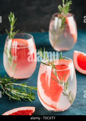 Infusa detox acqua o bevande alcoliche o analcoliche cocktail con succo di pompelmo e rosmarino in vetro sul verde e nero lo sfondo di cemento. Il mangiare sano o vacanza bere concetto, copia spazio per il testo Foto Stock