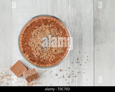 Cioccolato budino di chia in vetro e cubetti di cioccolato slice grigio su un tavolo di legno. Vegano sana colazione con copia spazio. Vista superiore o flat-lay. Foto Stock