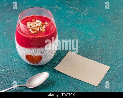 Idea per una sana prima colazione il giorno di San Valentino: Chia pudding con bacca rossa, purea di mandorle tritate sulla sommità e fragola a forma di cuore. Con vuoto valentines biglietto di auguri per il testo Foto Stock