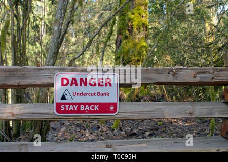 Il bianco e il rosso il pericolo della lettura del segno della banca in sottosquadro stare indietro montato su una struttura di guardrail staccionata lungo un sentiero in Kanaka Creek Parco Regionale, B. C. in Canada. Foto Stock