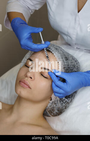 Cosmetologia estetica. Facelift in spa salone. Estetista iniezione facendo la ragazza brow pieghe. La levigatura le rughe del viso. Close-up Foto Stock