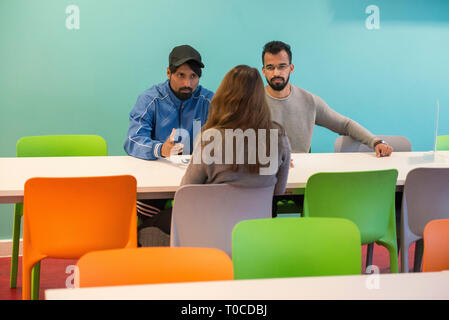 Un gruppo di giovani studenti stranieri in seduta il collegio mensa a chattare e socializzare gli uni con gli altri in una felice e divertente Foto Stock