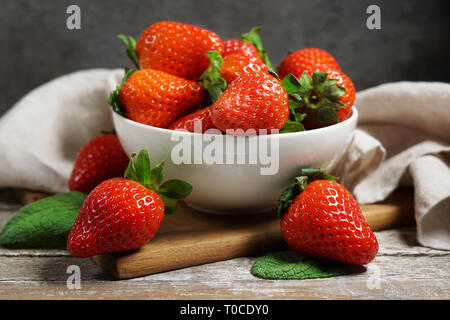 Concetto di fragola con un gruppo di ripe rosso le fragole in un recipiente bianco vicino la vista frontale su un vintage tavola in legno rustico in background. Foto Stock