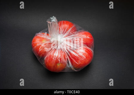 Busta di plastica chiusa con pomodori rossi nel centro di uno sfondo grigio. Foto Stock