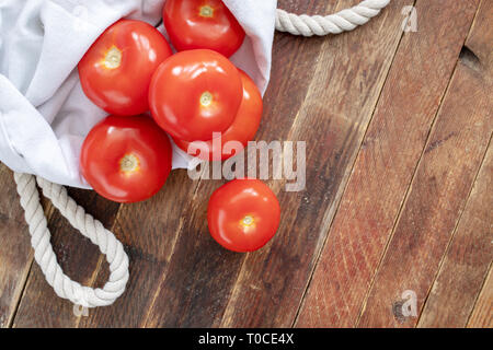 Close-up pomodori rossi in eco-friendly riutilizzabile di lino bianco borsa sul tavolo di legno. Foto Stock