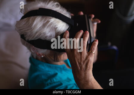 Disattivato Attiva donna senior utilizzando la realtà virtuale testa sulla sedia a rotelle in camera da letto a casa Foto Stock