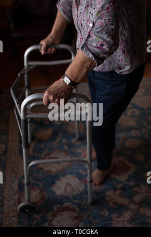 Attiva donna senior a piedi con walker nel salotto di casa Foto Stock
