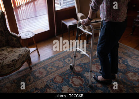 Attiva donna senior a piedi con walker nel salotto di casa Foto Stock