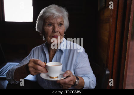 Considerato attivo senior donna che guarda lontano mentre avente il caffè a casa Foto Stock