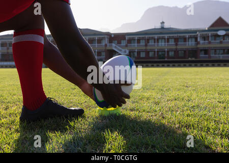 Maschio di giocatore di rugby immissione rugby palla su uno stand nel parco giochi rugby Foto Stock