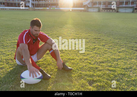 Rugby maschio giocatore seduto con palla da rugby nel terreno Foto Stock