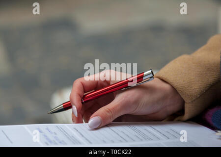 Una immagine di una mano e di una penna della compilazione di un modulo. Donna mani con manicure pastello con la penna. L'occupazione. Documento firma Foto Stock