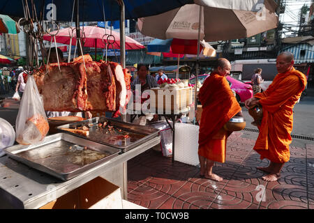 Due monaci buddisti durante la loro mattinata alms in giro per il vecchio mercato area di Chinatown, Bangkok, Thailandia, in piedi accanto a una pressione di stallo di carne Foto Stock