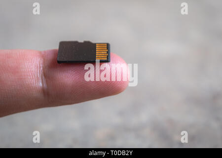 Una scheda di memoria Micro SD rispetto alle dimensioni di un dito Foto Stock