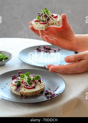 Tavolo con sani panini con ricotta, ravanelli e micro (verdi) cavoli e la donna mani tenendo un sandwich Foto Stock