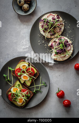 Panini sani con avocado, pomodoro, uova di quaglia, ravanelli e micro verdi (i germogli) su uno sfondo scuro, flatlay Foto Stock