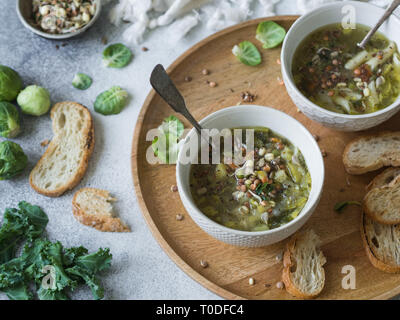 Vegetali verdi zuppa vegana da keil, i cavoli di Bruxelles, zucchine, porro con vari semi germinati e i germogli con crostini sul vassoio di legno sulla luce b Foto Stock