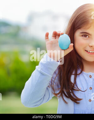 Ritratto di un simpatico baby girl tenendo in mano il blu decorato uovo, molla straordinaria giornata soleggiata, poco uova hunter, happy Easter egg hunt Foto Stock