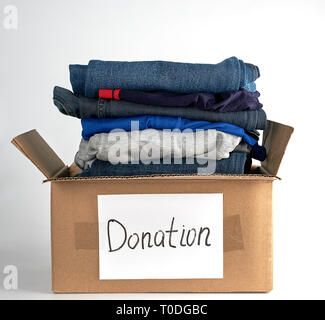 Panni ripiegati in un marrone scatola di carta con la scritta donazione su uno sfondo bianco, il concetto di aiutare le persone nel bisogno Foto Stock