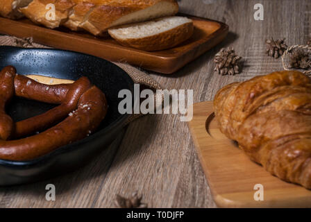 Cornetti freschi e salatini con baguette di pane posti su un vassoio e un tagliere di legno posto su una tavola di legno Foto Stock